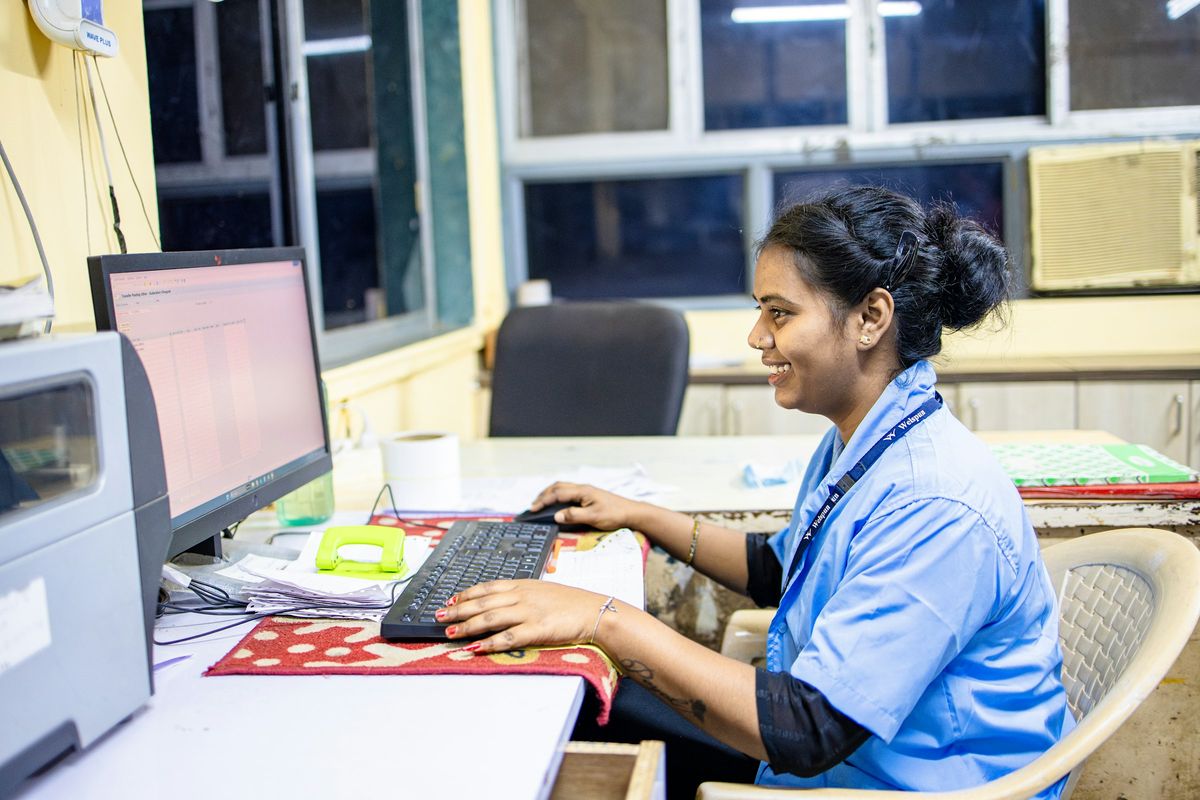 A nurse in a blue uniform smiling while working at a computer