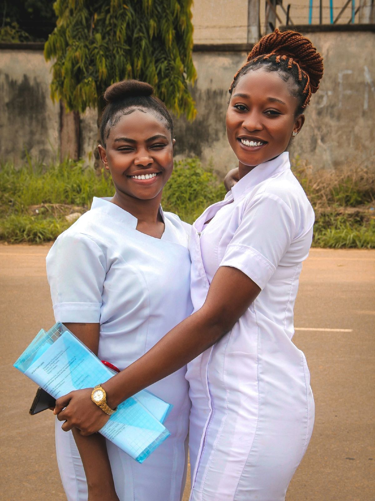 Two nurses in white uniforms smiling and hugging outdoors